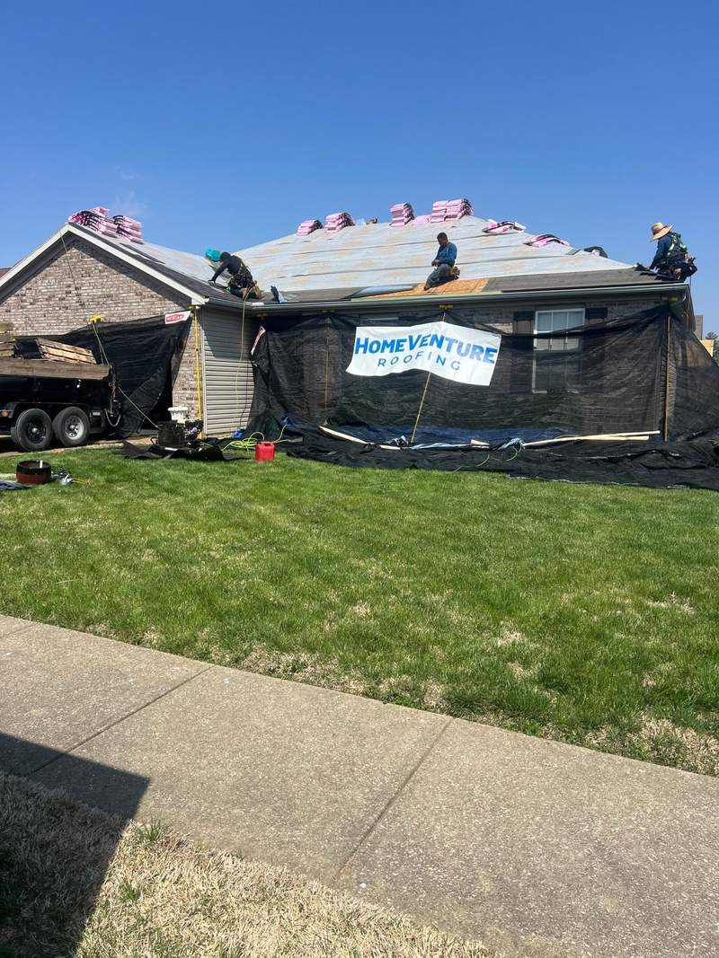 Brick house with pink shingle stacks on the roof and dump trailer ready in Evansville.